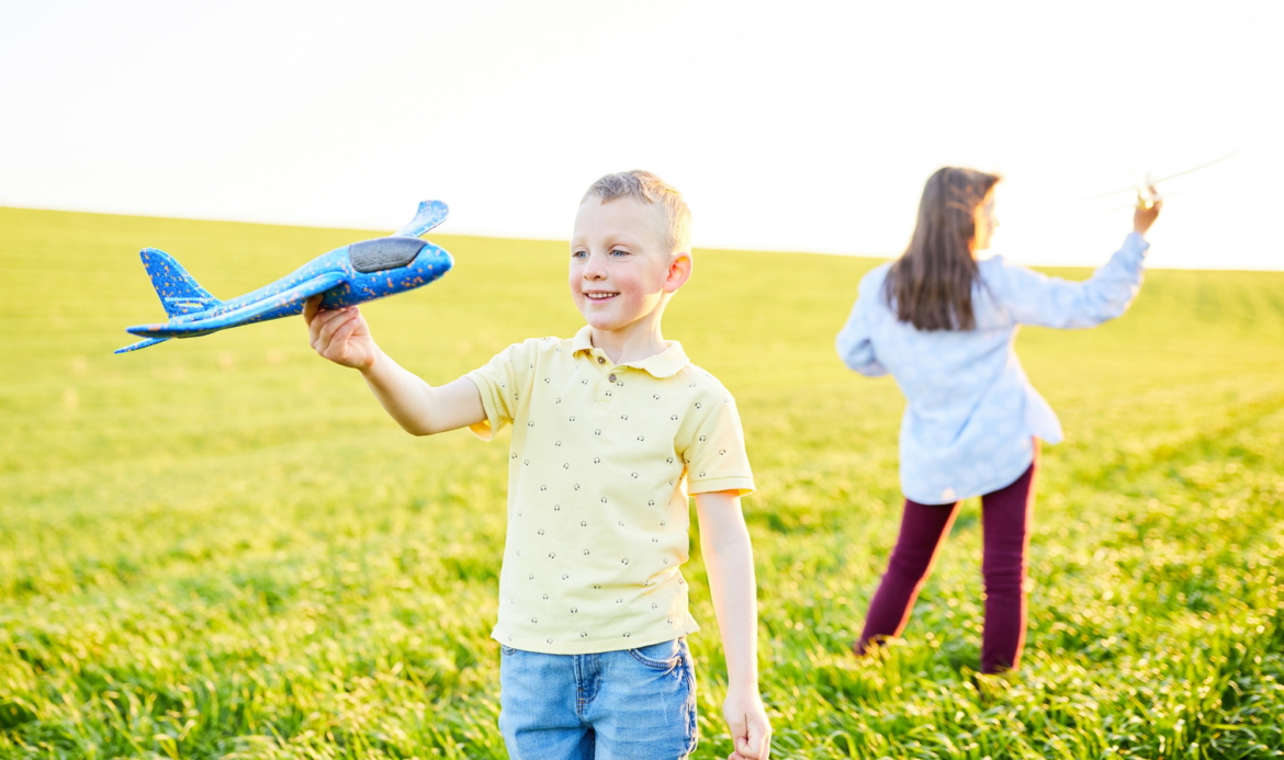 Children play in the field and imagine themselves to be pilots on a sunny summer day