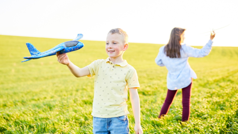 Children play in the field and imagine themselves to be pilots on a sunny summer day